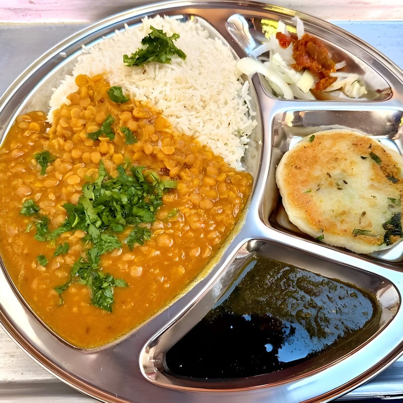 Pakistani thali with dal, rice, flatbread, chutney, and pickled onions on a metal tray.
