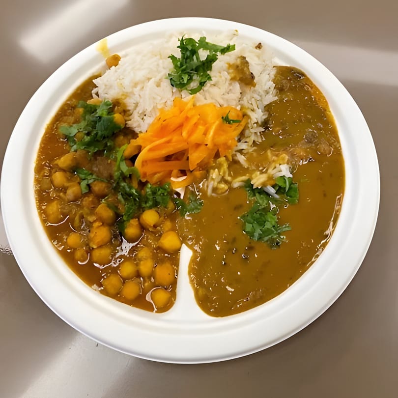 Pakistani food plate with rice, chana masala, and dal, garnished with cilantro and pickled carrots.
