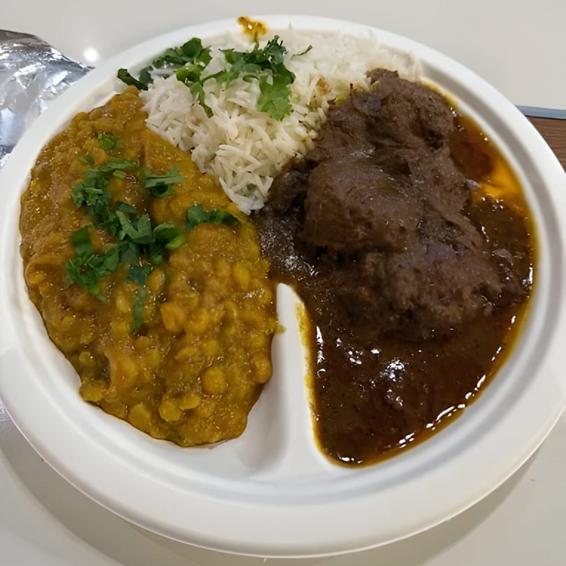 A white plate with three sections: yellow lentil curry, white rice with cilantro, and brown meat curry.