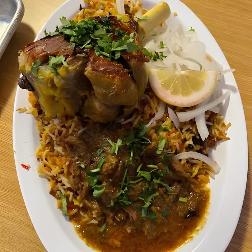 A large plate of Pakistani lamb shank biryani with rice, curry, onions, lemon, and cilantro.